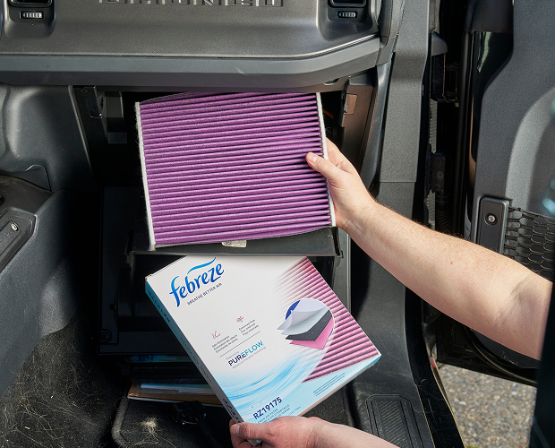 Person holding a Febreze air filter and packaging inside a vehicle.